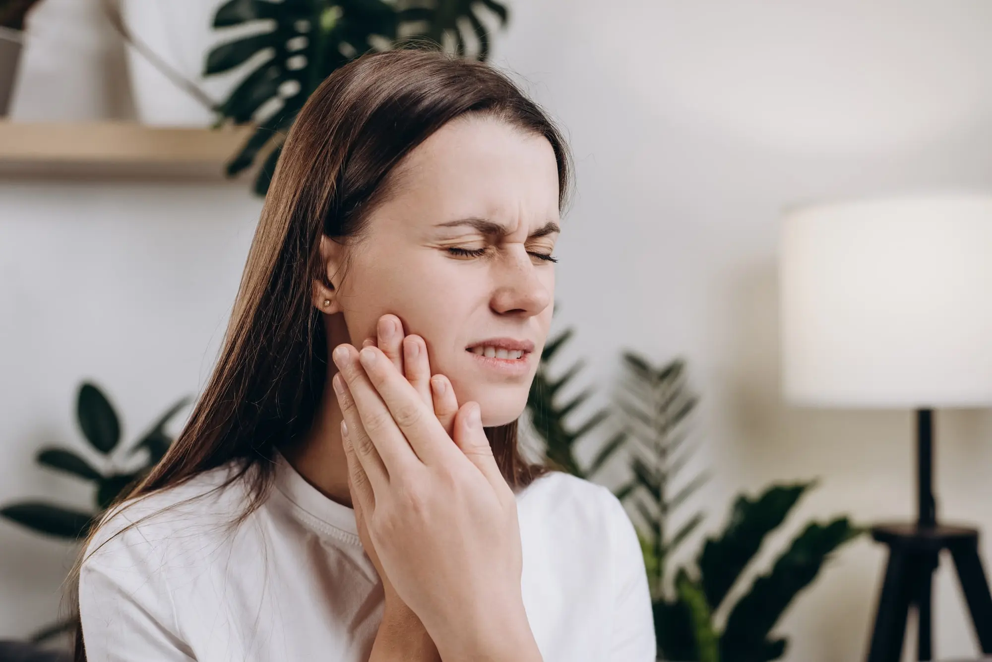 A-young-woman-holding-her-hand-to-her-cheek-wincing-in-pain-after-tooth-removal