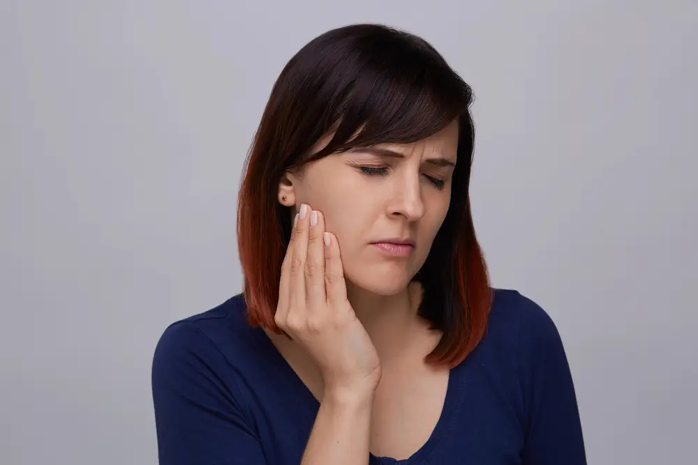 A woman holding her hand to her cheek while wincing in pain