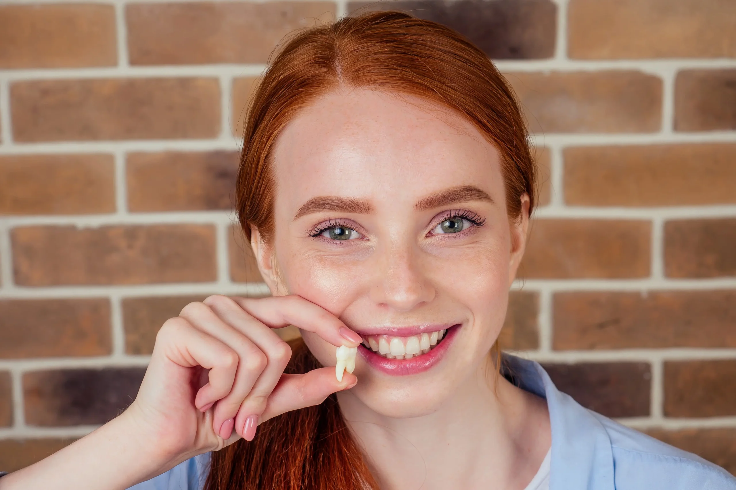 A young girl smiling while holding a tooth in her hand.