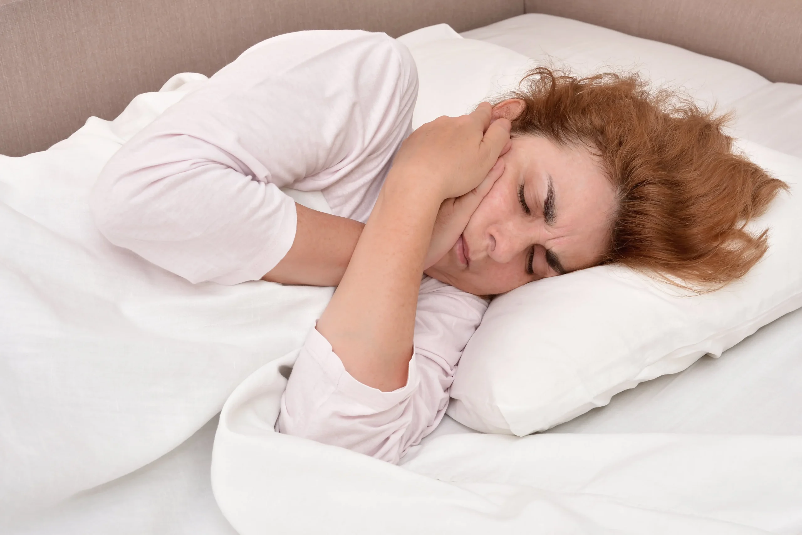 Woman lying in bed holding her hand to her cheek in pain