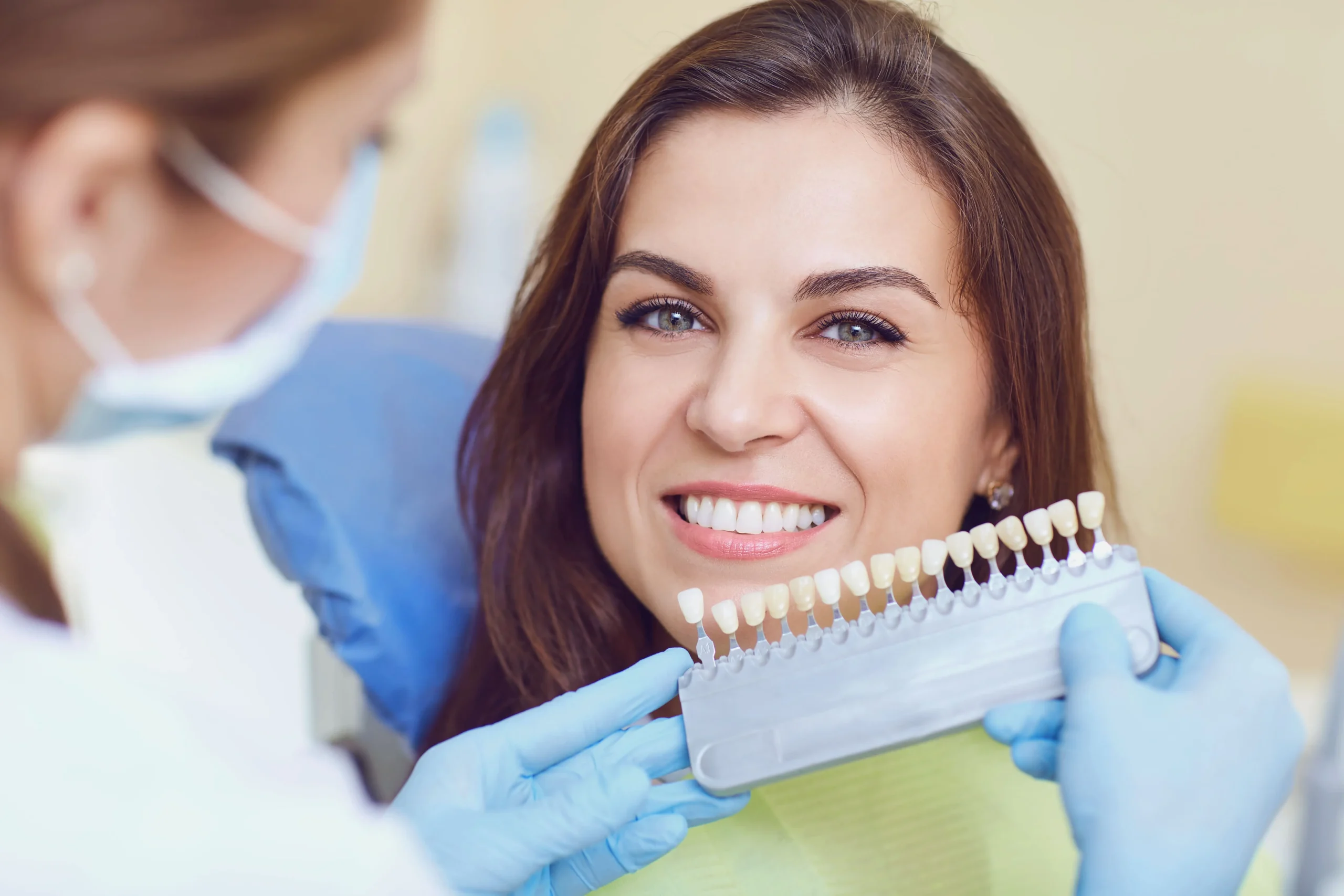 A lady smiles while the dentist matches her teeth to a colour chart