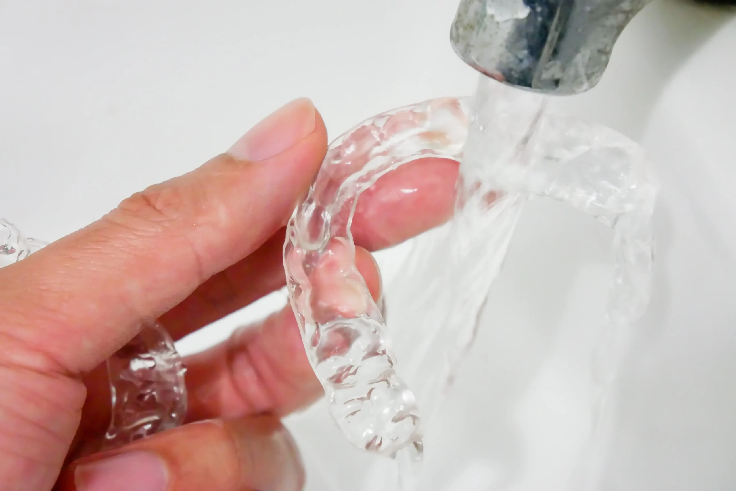 A person holds an invisalign retainer under a running tap